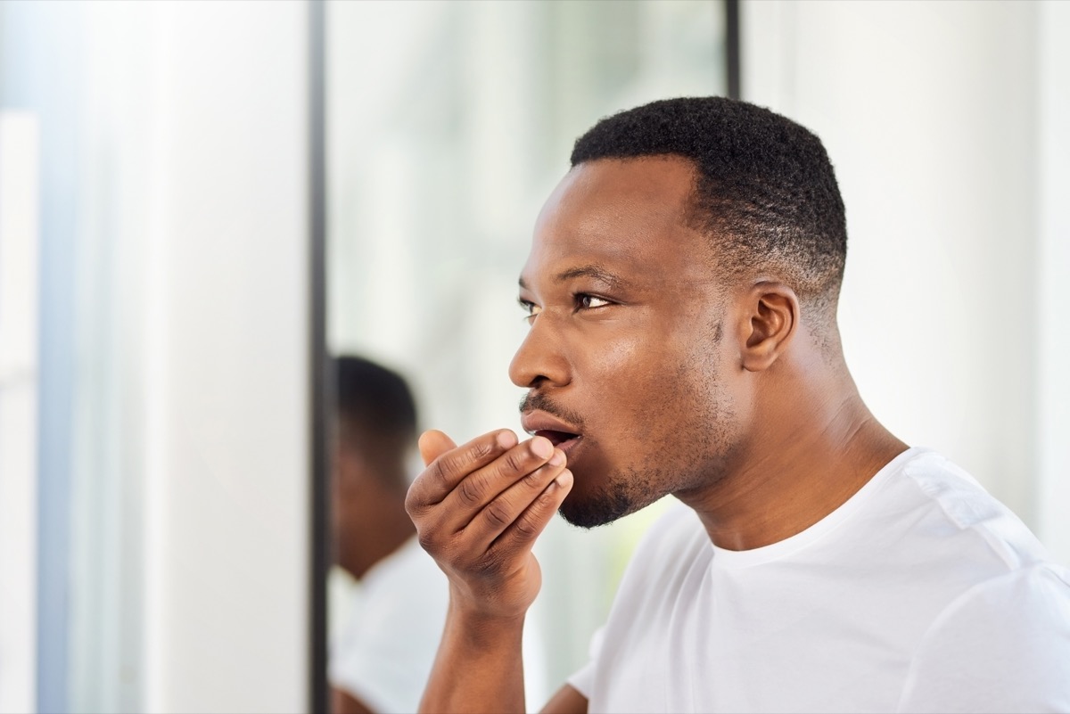 A young man looks in the mirror while smelling his breath