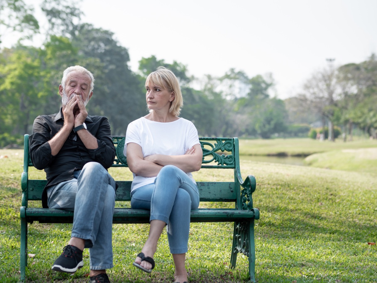 Senior couple having problems in the park, both have legs crossed