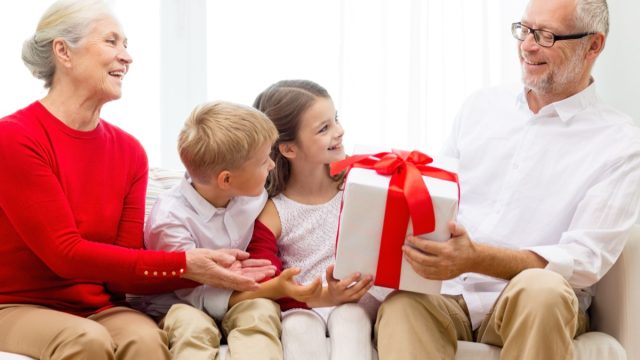 white grandparents getting gifts from their two grandkids on couch