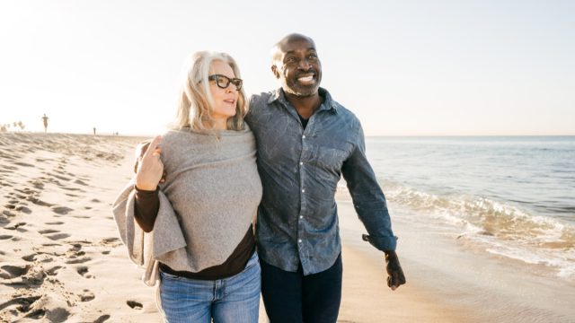 older couple walking on the beach with their arms around each other