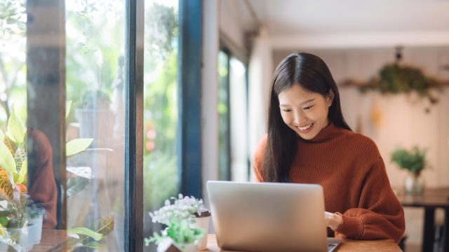 young asian woman smiling and looking at her laptop at a coffee shop