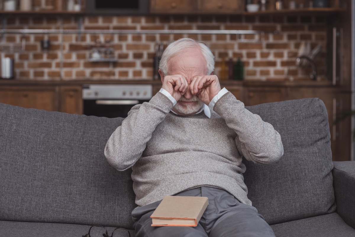 older white man rubbing his eyes on the couch