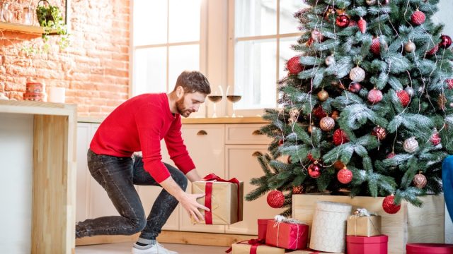 Man putting gifts under the Christmas tree preparing for a New Year holidays at home