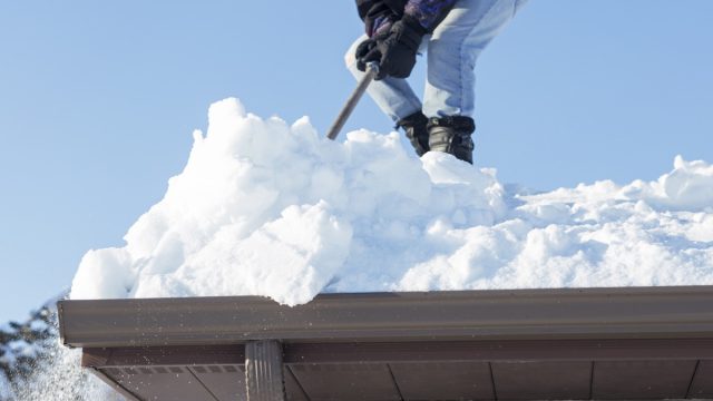 man scraping snow off roof