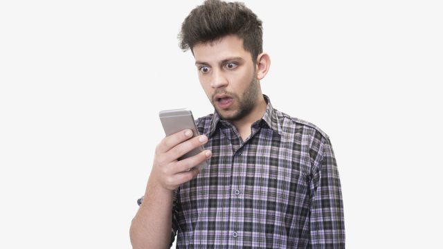 Close-up portrait of shocked young man looking at smart phone's screen receiving bad news on a white background