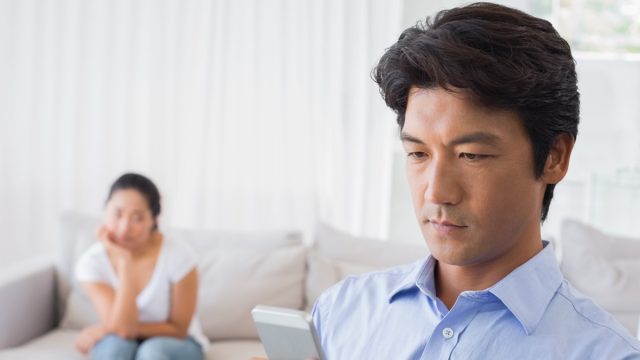 man on phone while upset wife looks on from bed