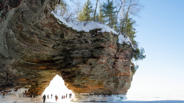 people walking underneath the rock formation on one of the apostle islands
