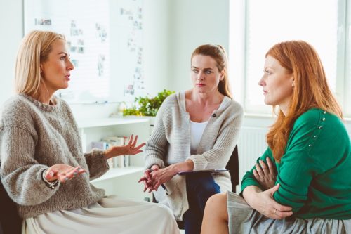 Mature female discussing problems during group therapy. Therapist is sitting with women in session. They are in wellness center.