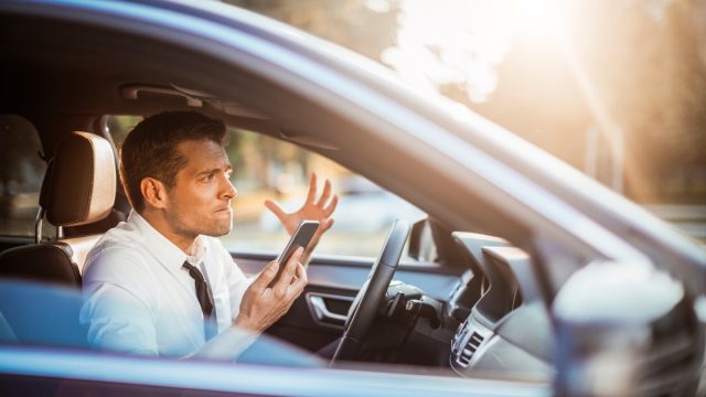 Close up photo of a businessman yelling at his phone while driving