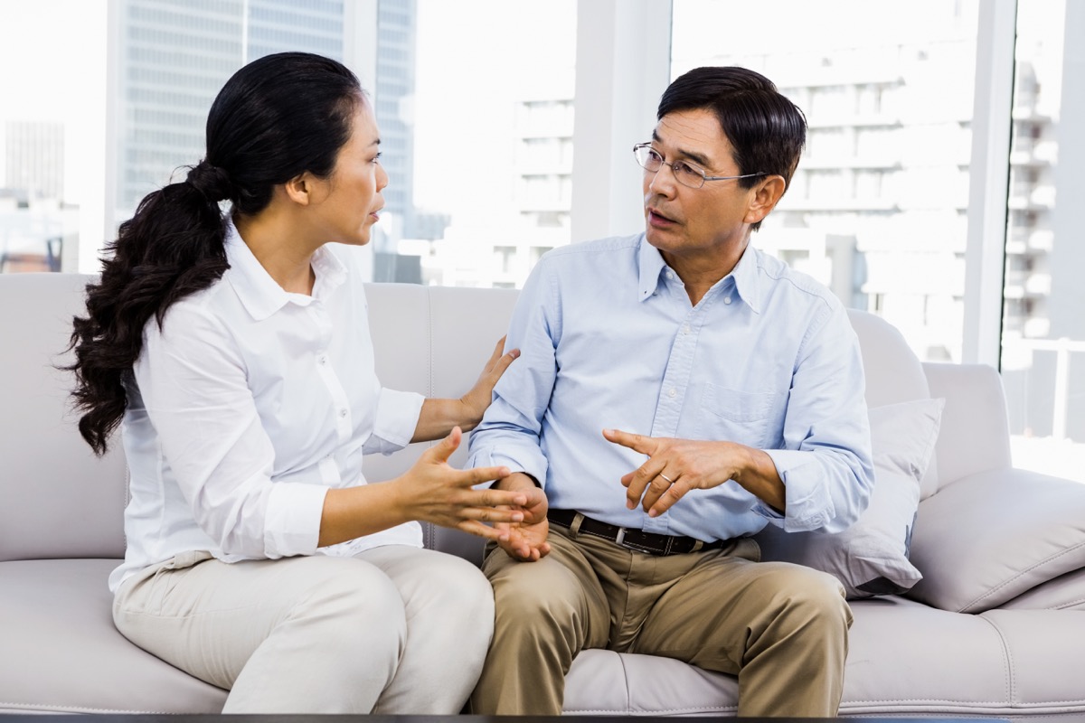 Concerned-looking woman and man sitting on grey couch with a city view