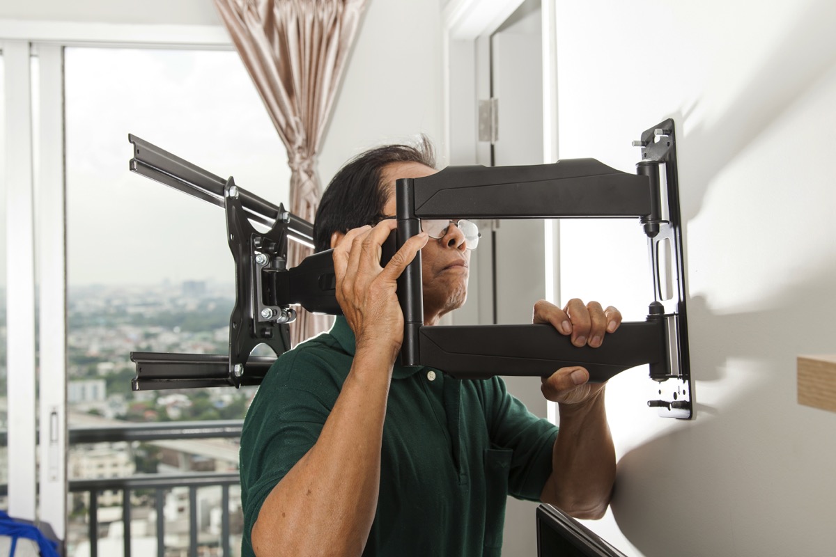 older asian man installing tv bracket on wall