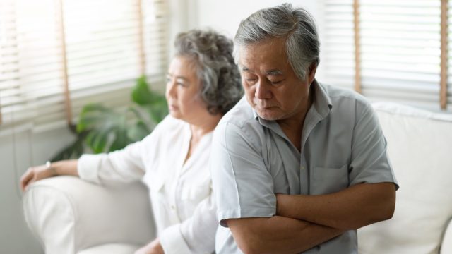 older asian couple sitting on couch looking upset and angry