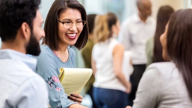cheerful young businesswoman stands with an unrecognizable coworker in a crowded office building and smiles as she shakes hands with her new unrecognizable client