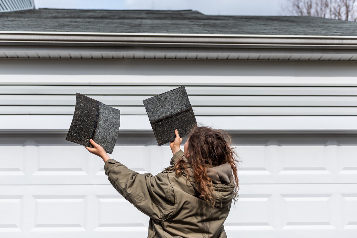 Female homeowner standing in front of house holding two roof tile shingles inspecting damage