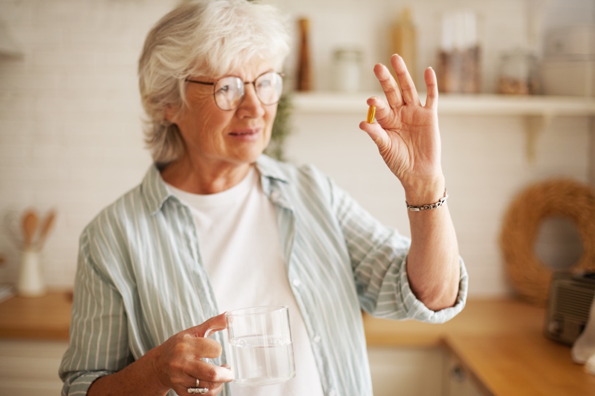 Senior woman holding a glass of water in one hand and a pill or vitamin in the other