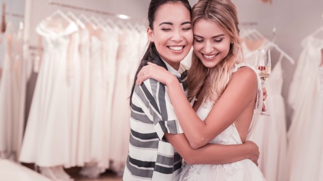 two women hugging in wedding gown and casual clothing at bridal shop