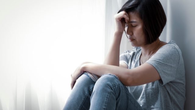 upset middle-aged asian woman sitting on floor