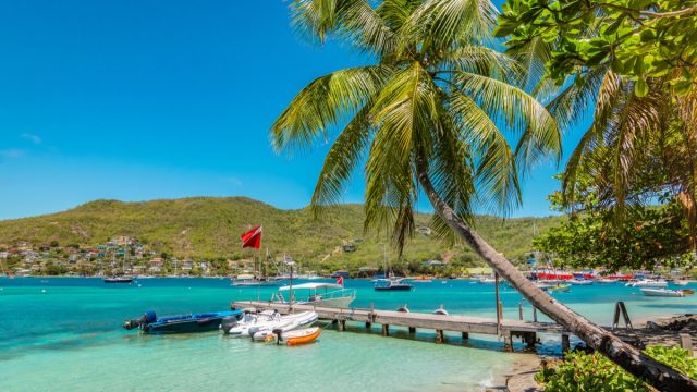 Bright and colorful image of Bequia. Palm trees at the water, blue sky and white clouds, boats in the harbor of Port Elisabeth. Saint Vincent and the Grenadines.