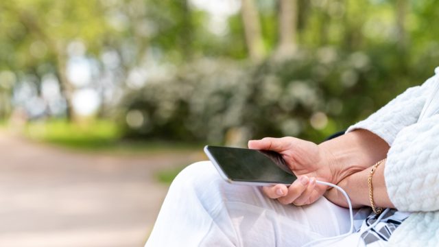 A senior woman with headphones is listening to music on her smart phone in the park