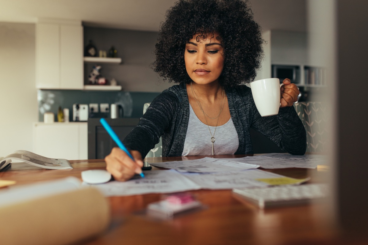 woman drinking coffee and taking notes while wfh on the computer