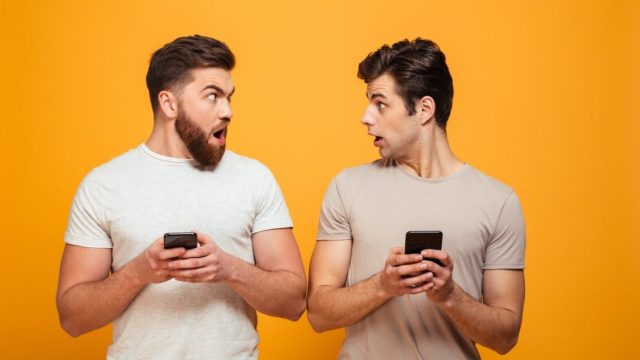 Two men holding phones and looking surprised
