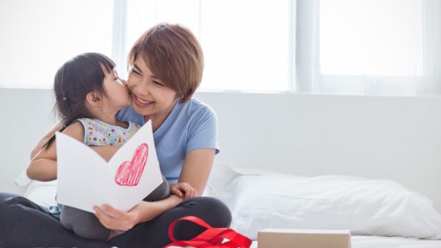 young asian girl giving mother card and kissing her on cheek