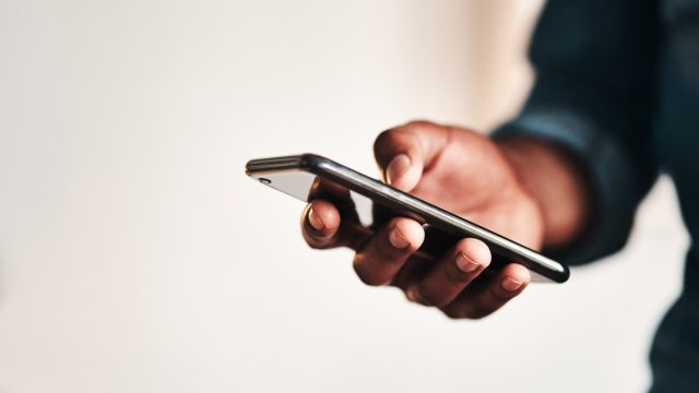 Cropped shot of an unrecognizable businessman standing alone in his home office and texting on his cellphone