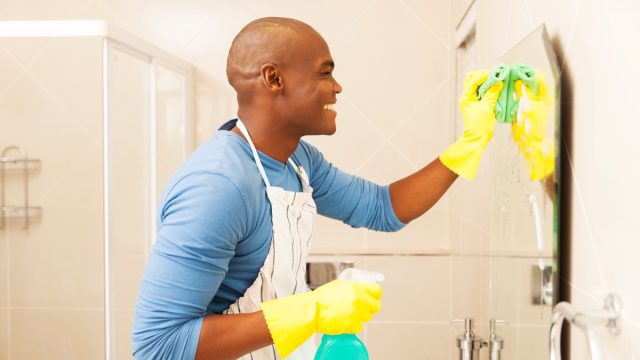 young happy black man cleaning bathroom mirror