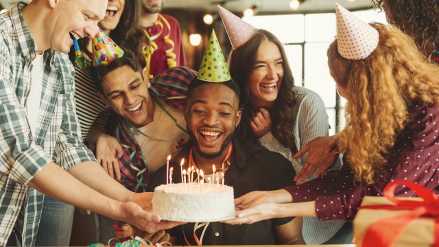 Happy black man celebrating his birthday, looking at cake with candles, surrounded by friends
