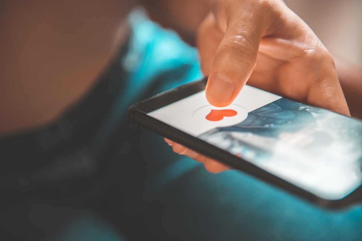 Finger of woman pushing heart icon on phone screen in dating app