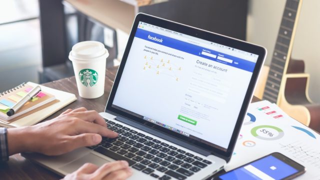 Person logging into Facebook on laptop at coffeeshop