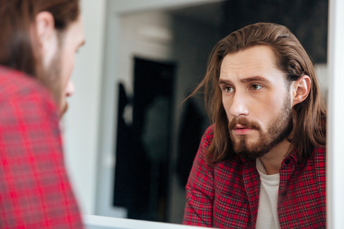 young bearded man looking seriously in the bathroom mirror