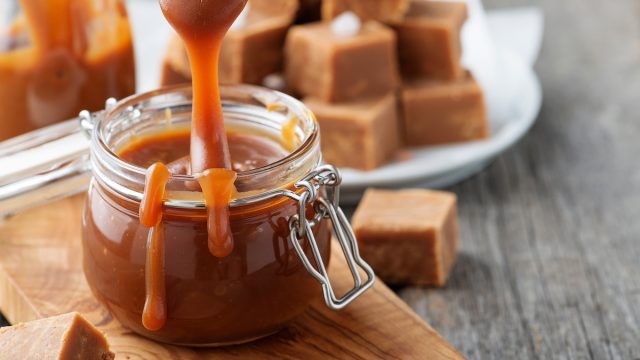 Homemade salted caramel sauce in jar on rustic wooden table.