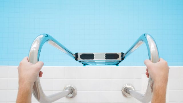 Man's hands holding on metallic ladder. Ready for swimming in the pool. Part of body. Point of view shot. Close up.