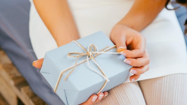 white hands opening ribbon on gift wrapped present