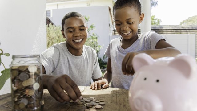 father throwing coins into a piggy bank with his daughter.