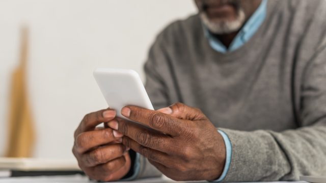 cropped view of senior man using smartphone while sitting at table