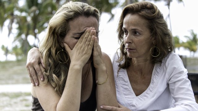 middle aged white woman comforts friend who is dealing with a loss, her head is in her hands