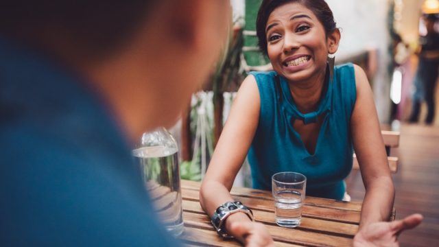 Young woman sitting in stylish cafe apologizing, gesturing and searching for an excuse to tell her boyfriend