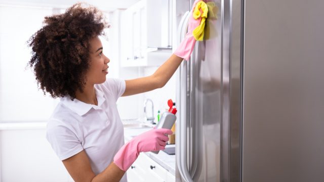 Woman cleaning fridge with gloves
