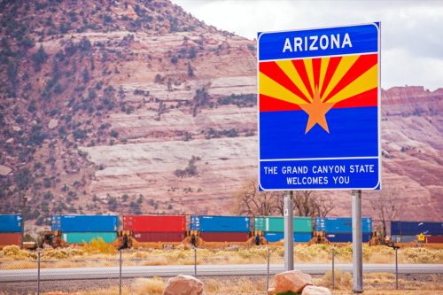 a blue "Arizona" sign off of the highway and in front of the Grand Canyon