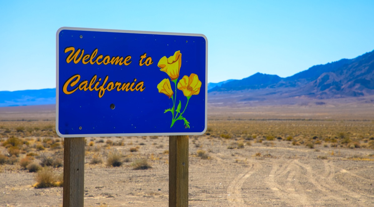 a blue "Welcome to California" sign on a dirt road