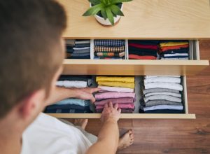 Organizing and cleaning home. Man preparing orderly folded t-shirts in drawer.