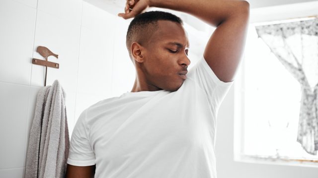 Shot of a young man smelling his underarms while standing in the bathroom