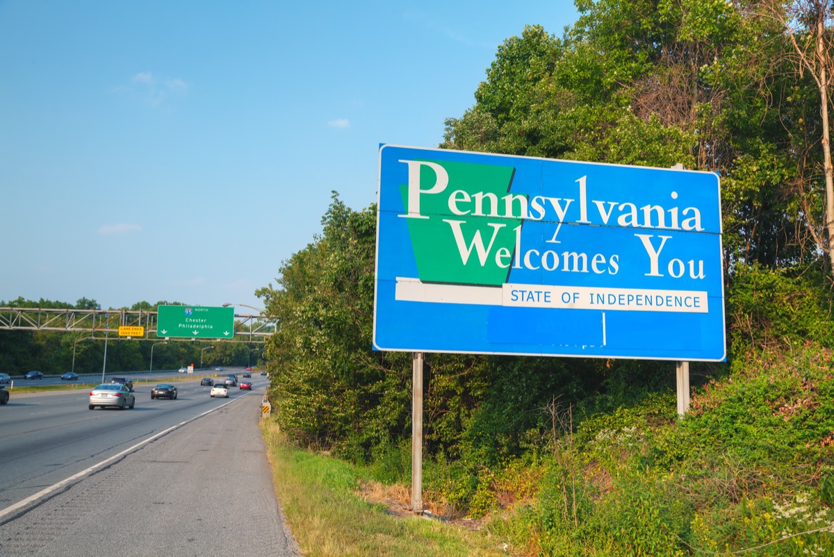 a blue "Pennsylvania Welcomes You" sign in front of trees and off a highway