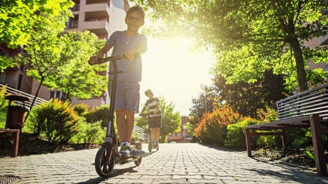 Kids riding scooters in city residential area. Sunny summer day.