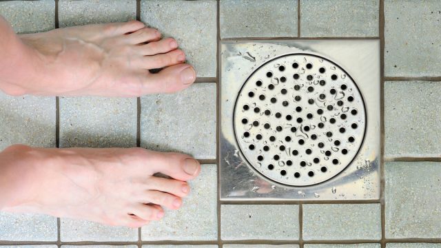 Feet in shower, closeup of floor and drain.