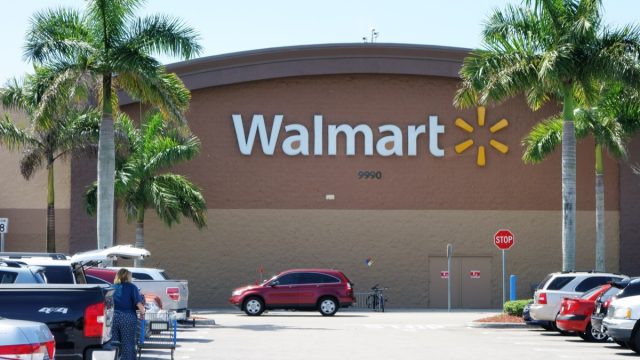 A Walmart store with a full parking lot. Walmart is the largest retailer in the world and operates thousands of large discount department stores. A woman customer empties her shopping cart into a car in the parking lot.