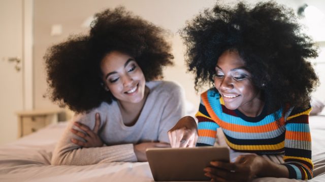 Friends using digital tablet in bed