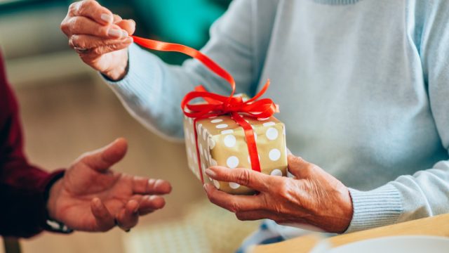 Close-up shot of a lovely senior couple exchanging christmas gifts in dining room.